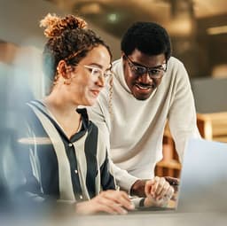 A pair of people looking at a lpatop working together to solve problems.